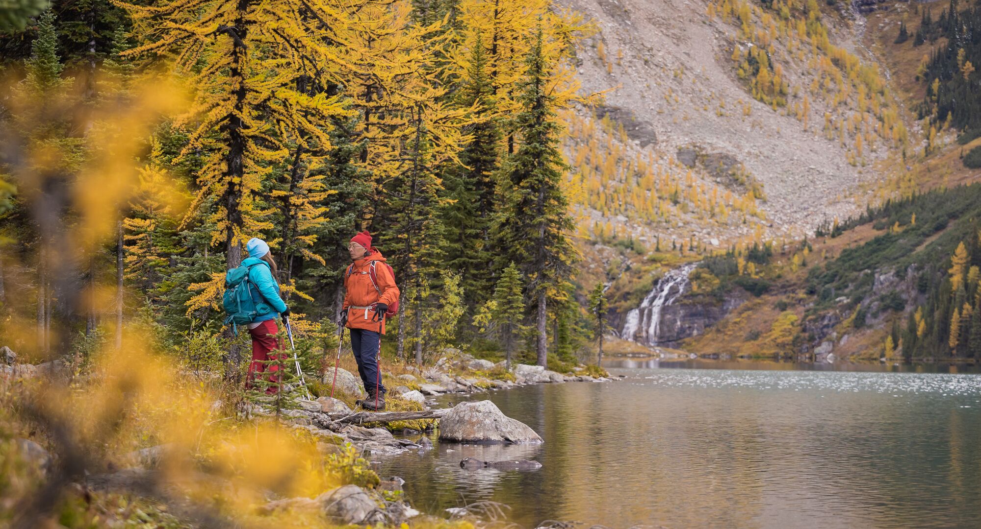 Two people stand on the edge of Taylor Lake in Banff National Park during larch season.